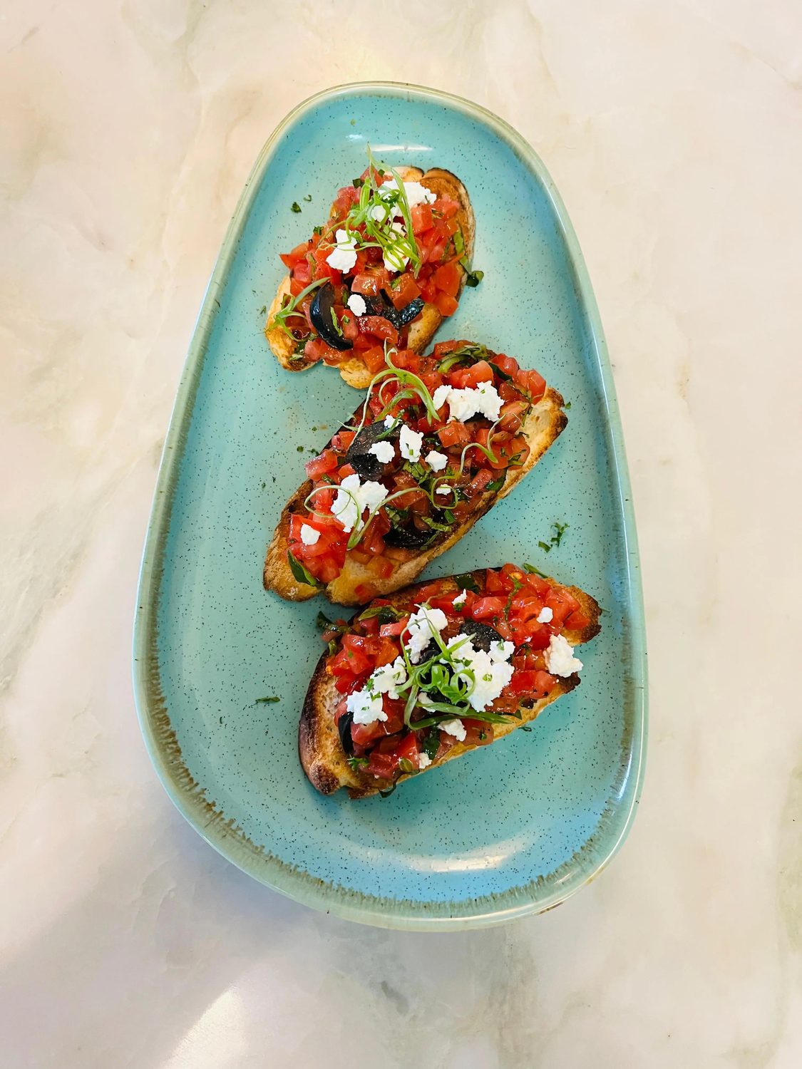 Three open toasts with tomato, feta and herbs on a blue platter
