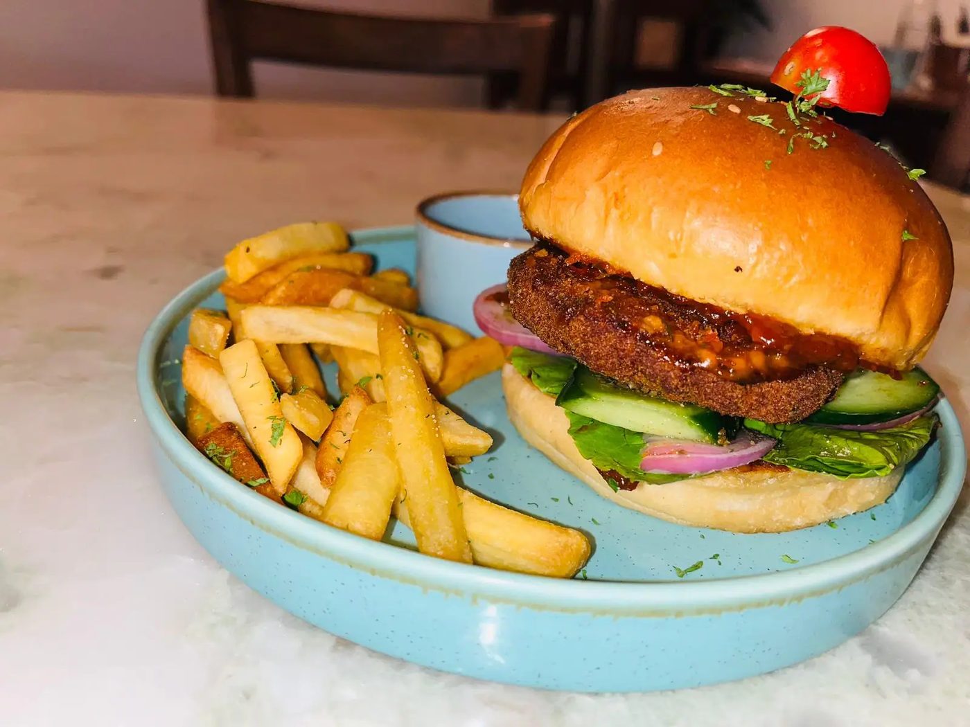 A burger with fries and dip on a pale blue plate