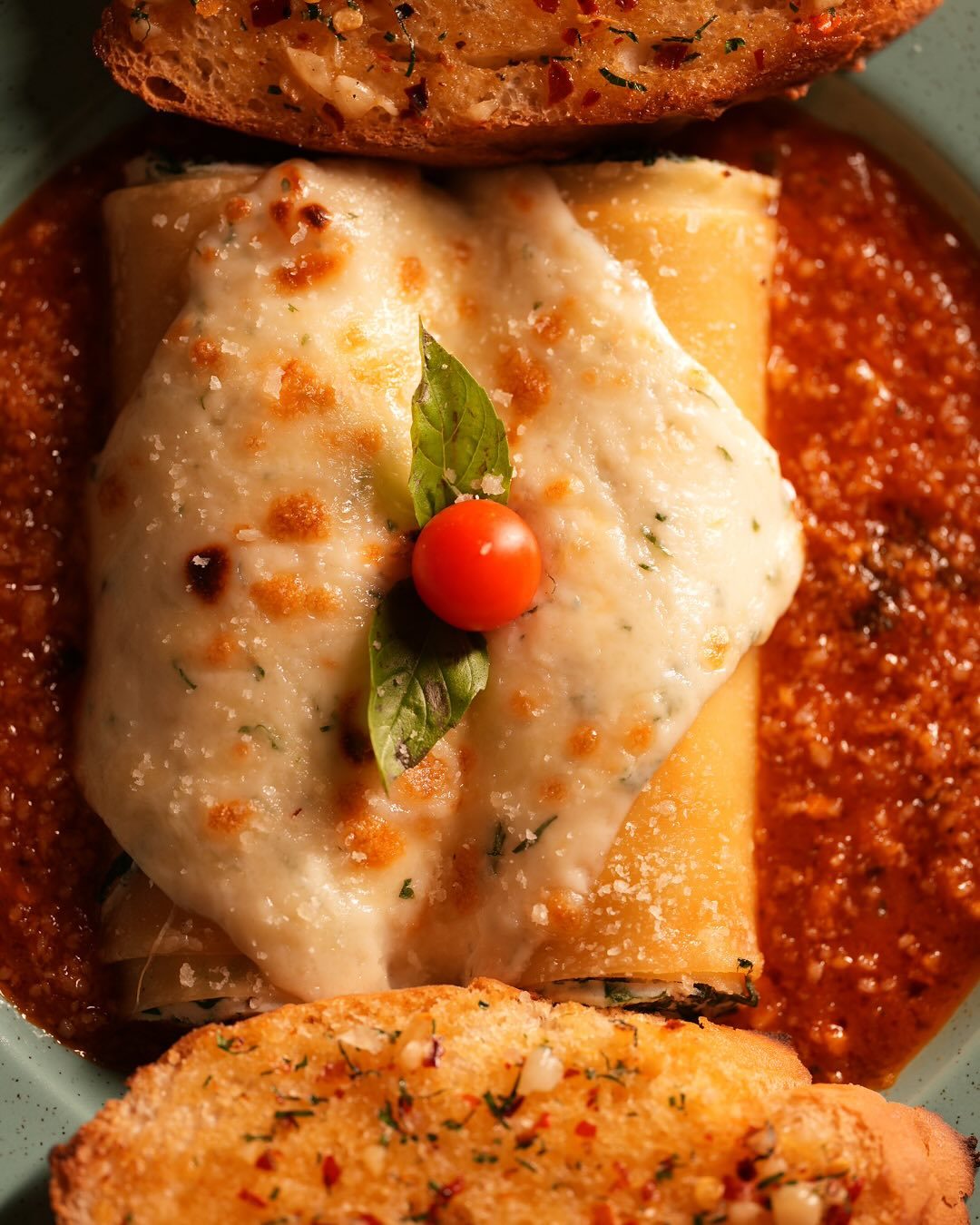Cannelloni baked in tomato sauce with melted cheese and garlic toast
