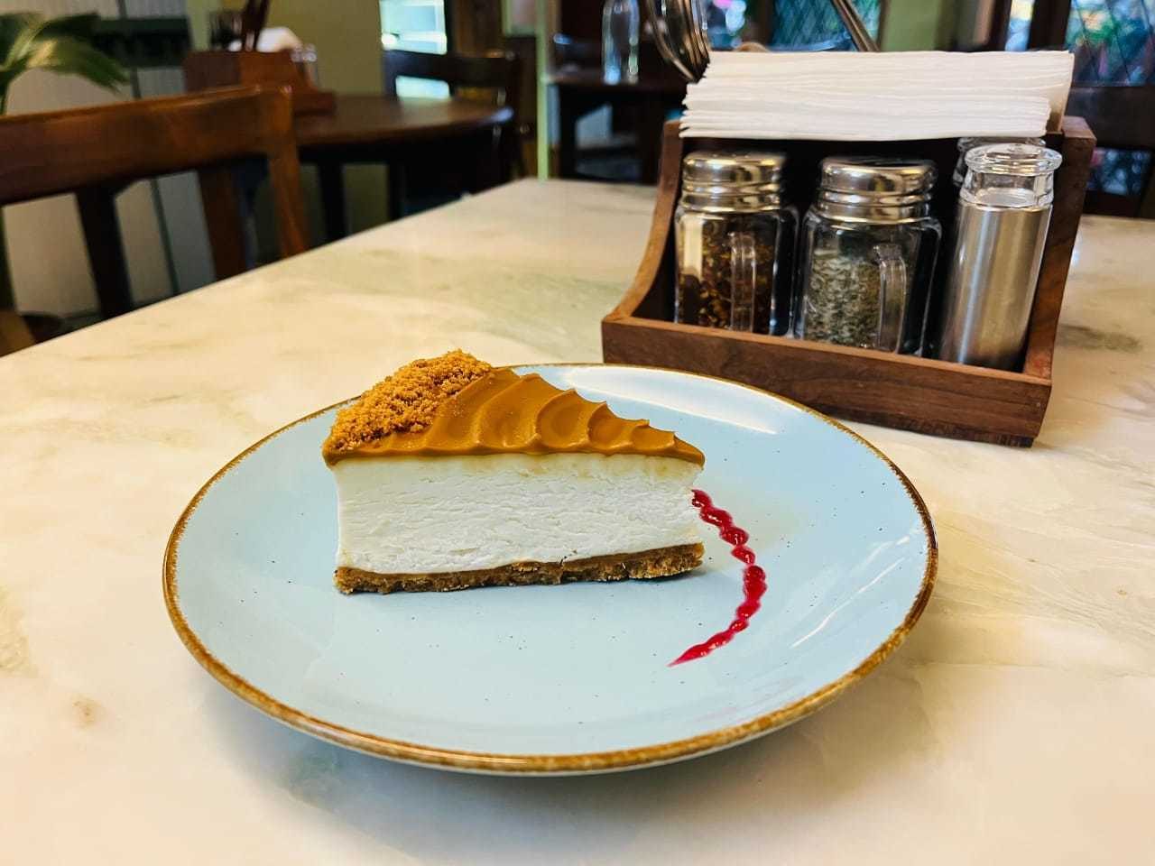 A slice of plain cheesecake on a pale blue plate with a berry coulis