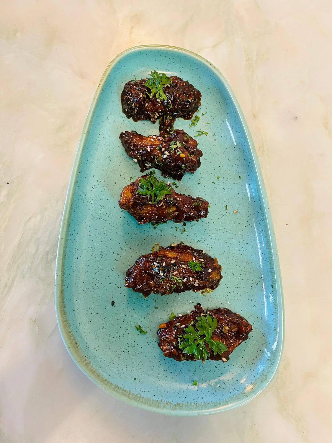 Four glazed chicken wings arranged on a green ceramic plate