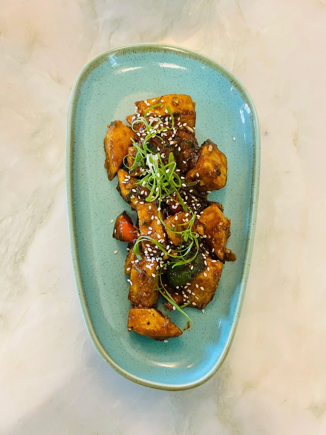 Glazed chilli paneer with sesame and micro greens on a green plate