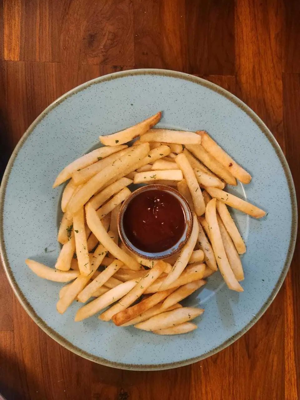 A plate of French fries with a pot of ketchup in the middle