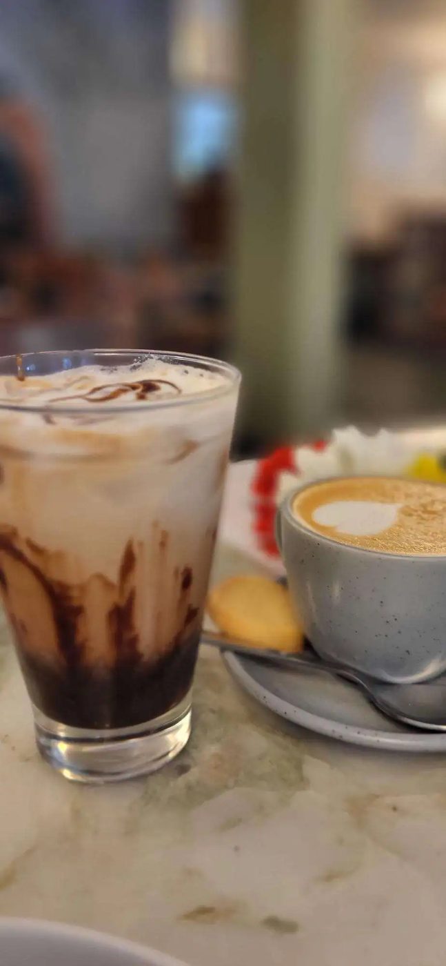 An iced chocolate coffee beside a cappuccino on a marble counter