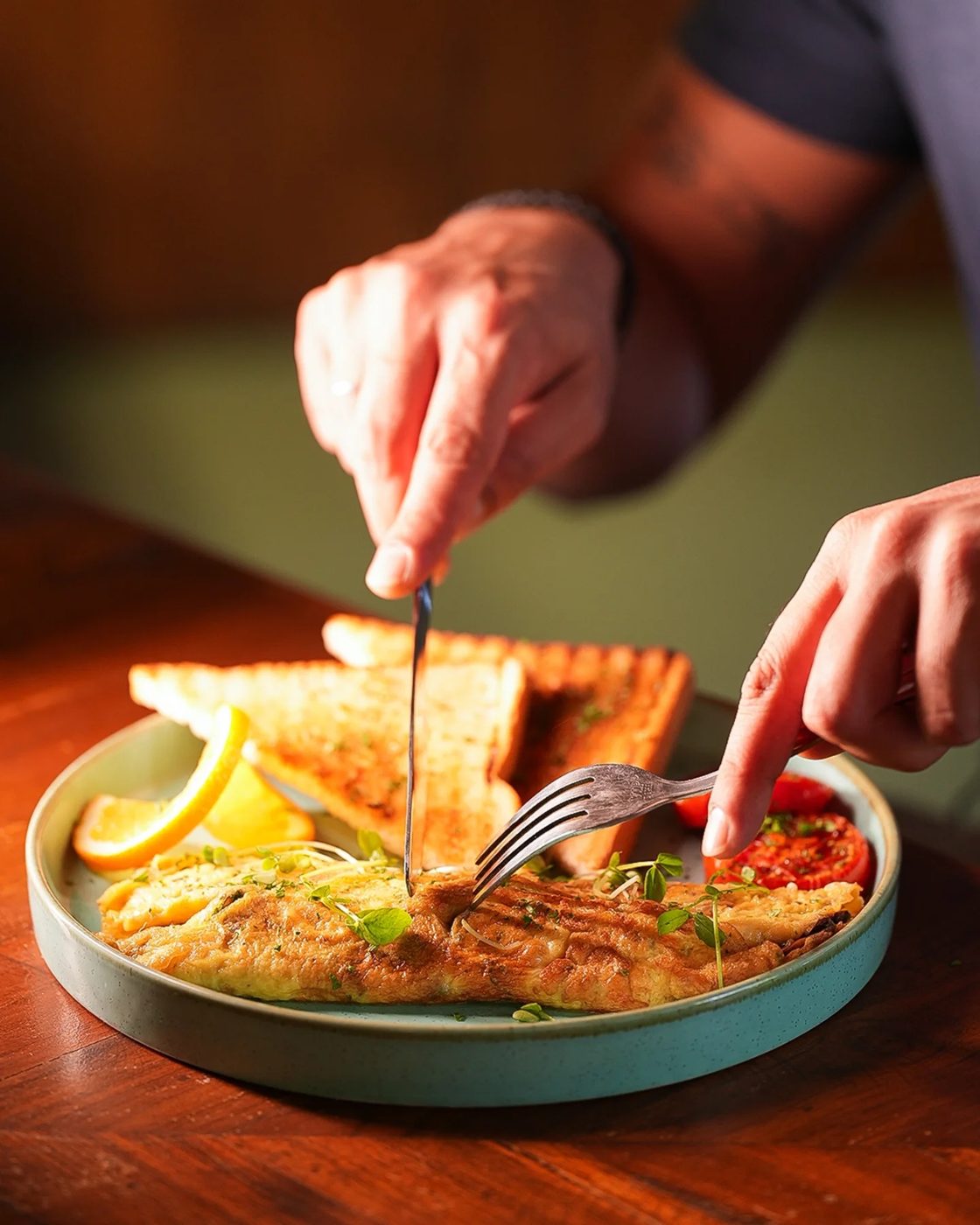 A herbed omelette with toast and grilled tomato being cut into