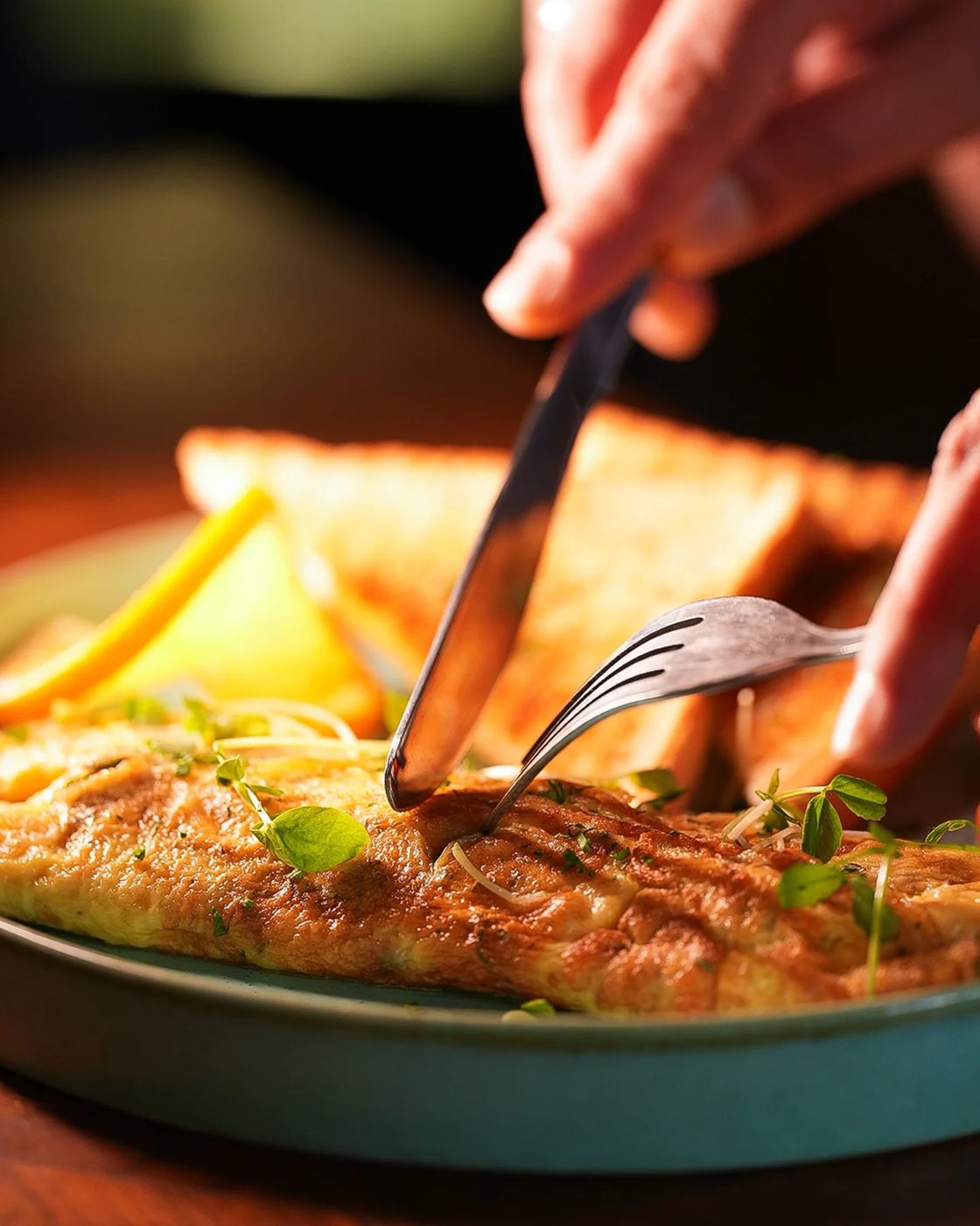 A knife and fork cutting into a herbed omelette served with toast