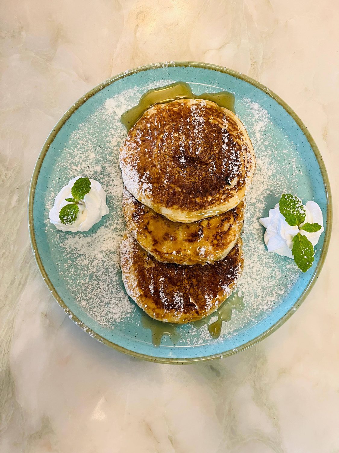 Thick pancakes dusted with sugar and topped with cream and mint
