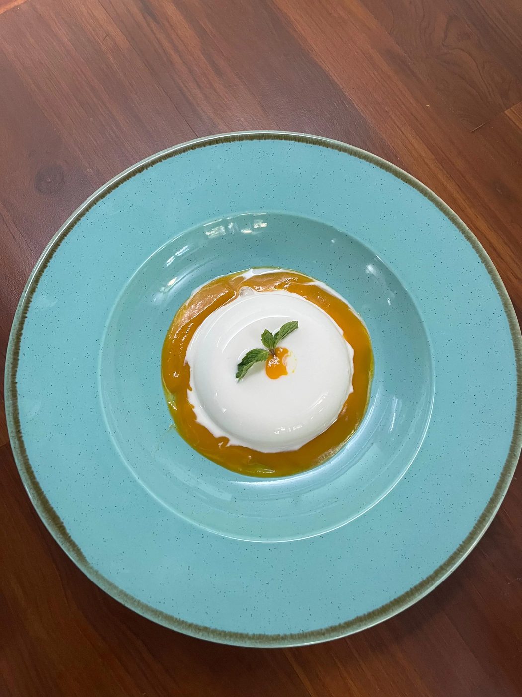 Set panna cotta on a pale blue plate with mango coulis and mint