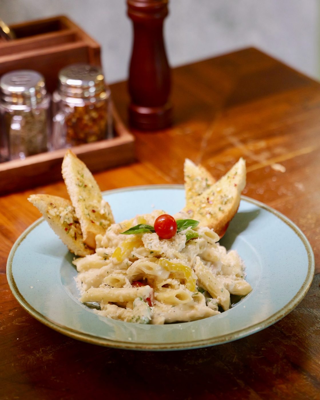 Creamy alfredo penne with garlic bread on a pale blue plate