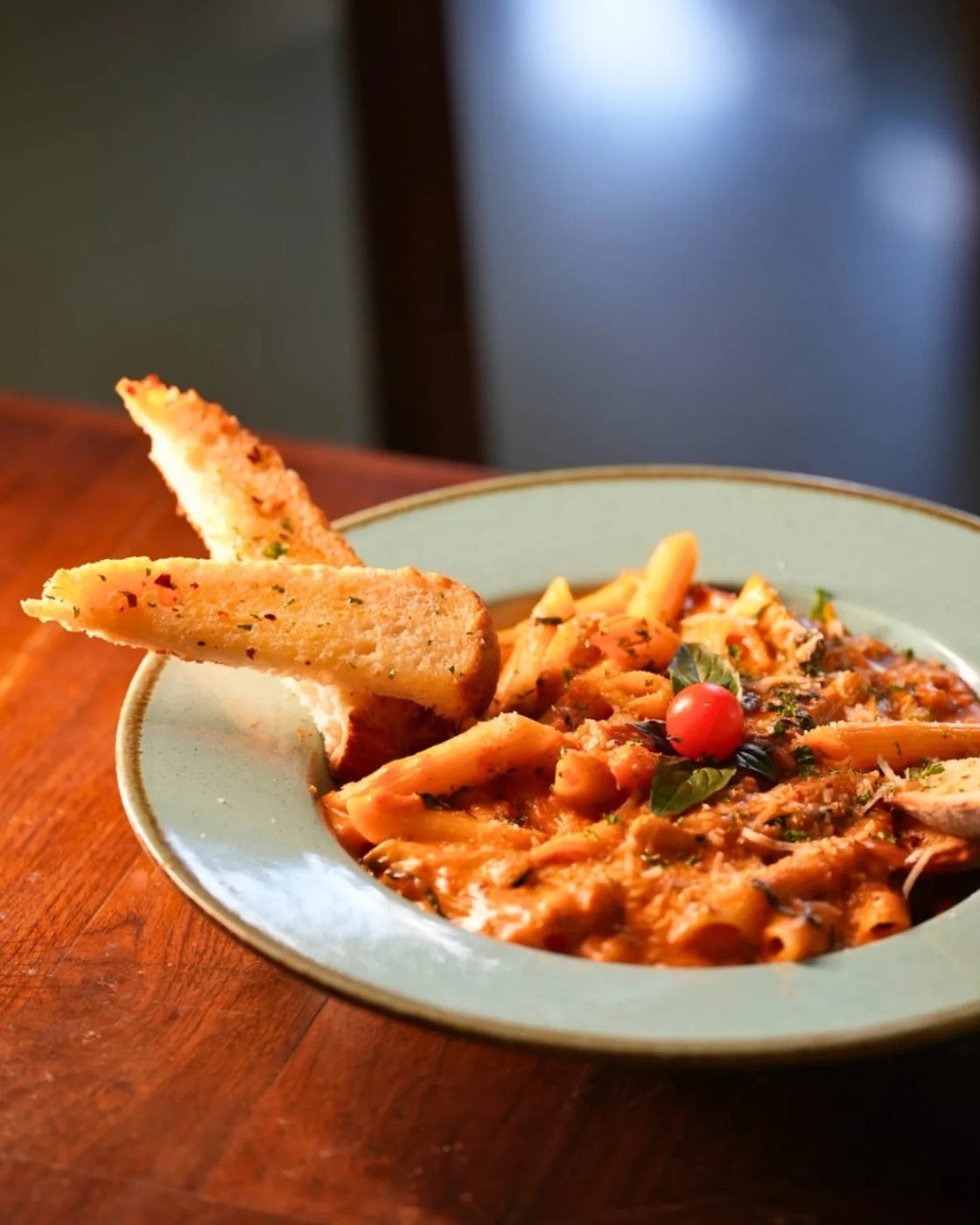 Penne arrabbiata with garlic bread on a green plate