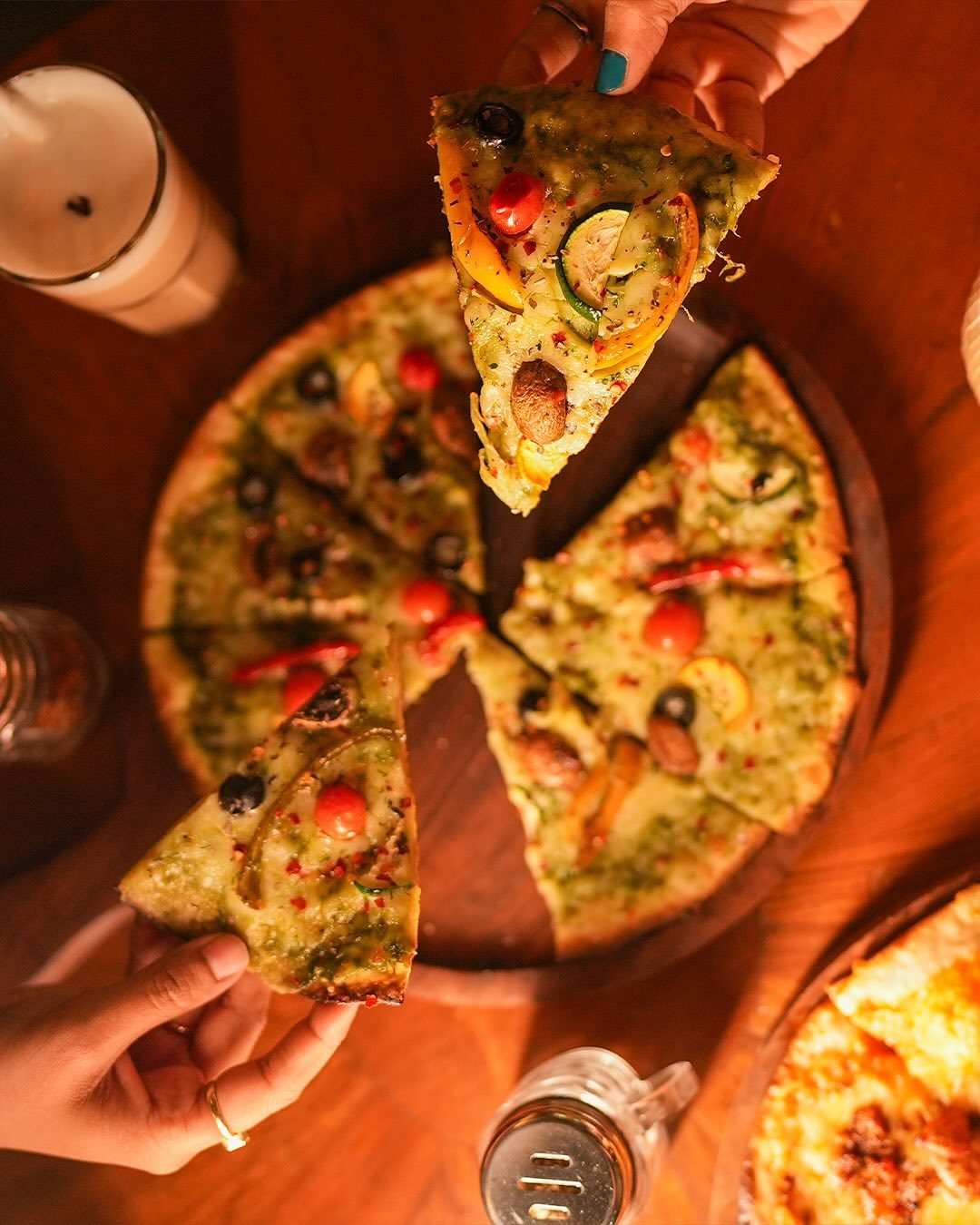 A pesto pizza on a wooden board with olives, cherry tomatoes and peppers