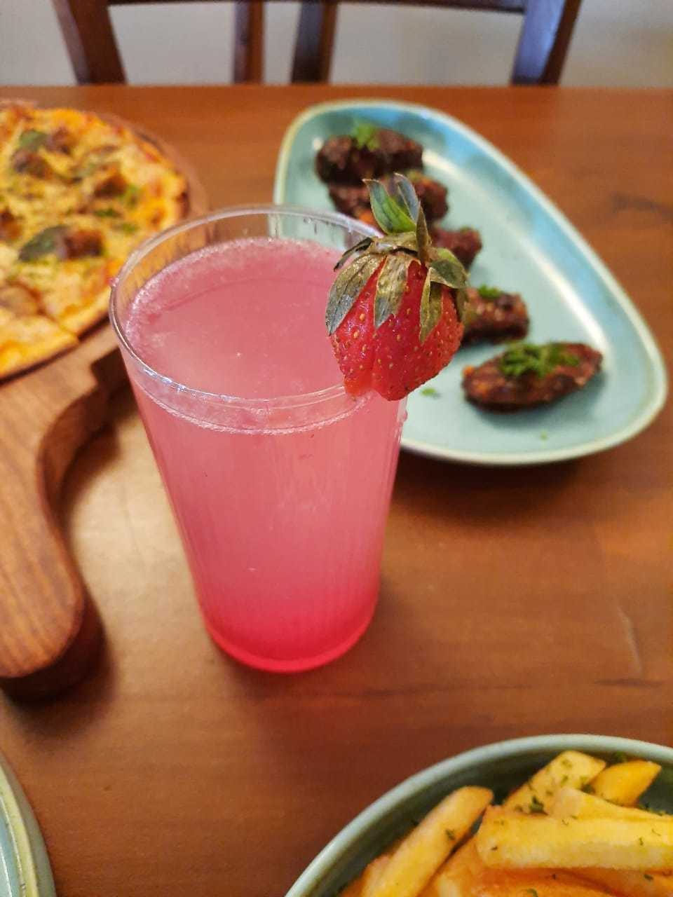 A pink strawberry cooler with a whole strawberry on the rim