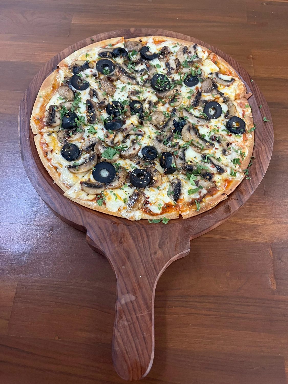 A mushroom and black olive pizza on a round wooden board