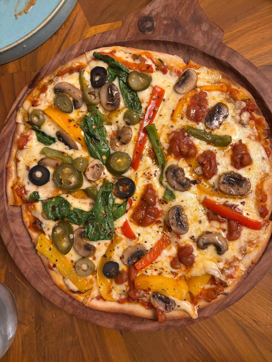 A loaded vegetable thin crust pizza on a round wooden board