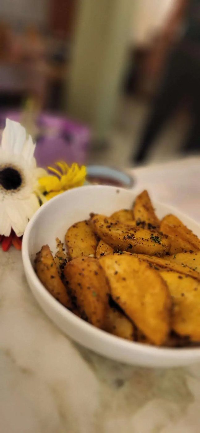 Herbed potato wedges in a white bowl beside fresh flowers