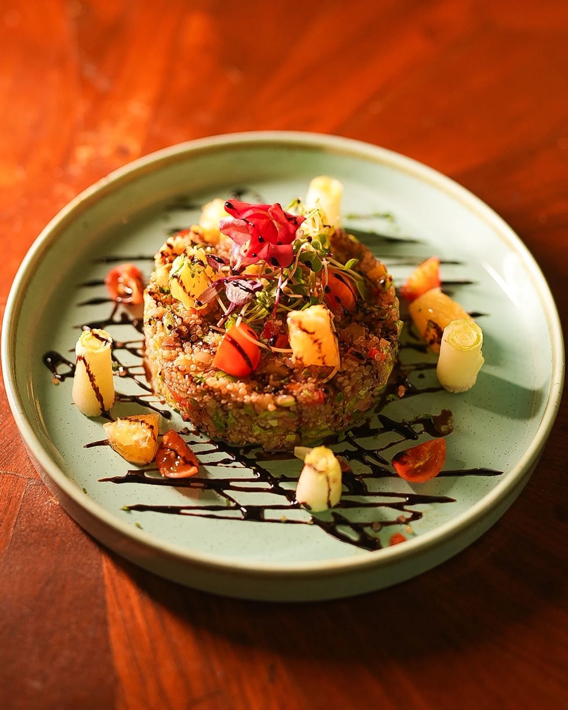 A quinoa cake plated with balsamic, peppers and micro greens