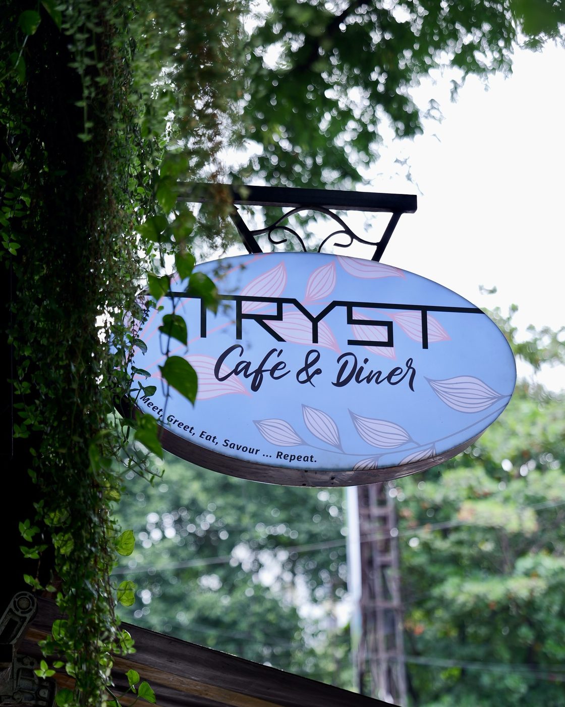 The TRYST Café and Diner signboard hanging among creepers