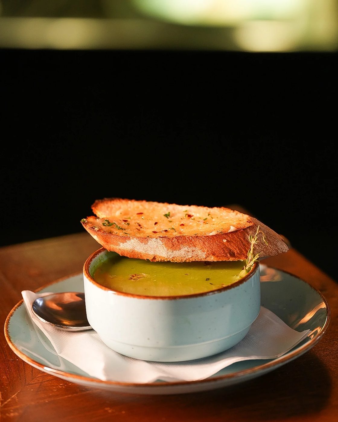 A cup of soup with a slice of herbed garlic bread balanced on top