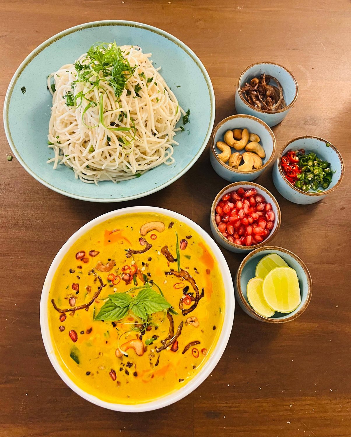 A yellow Thai curry with rice noodles and small bowls of condiments